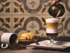 graos de café, pão e taça de capuccino sobre a mesa