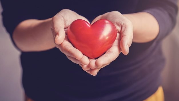 imagem de maos segurando um objeto no formato de coracao vermelho
