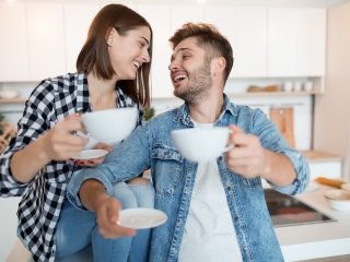 casal de mulher e homem sorrindo um para outro com xícara de café na mão