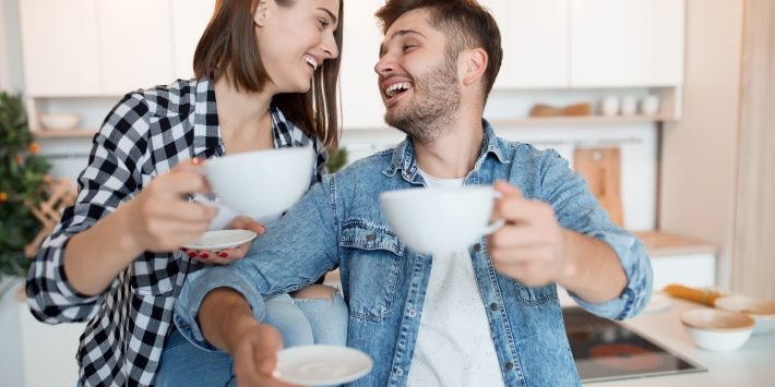 casal de mulher e homem sorrindo um para outro com xícara de café na mão
