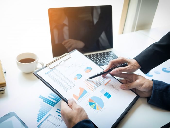 imagem de homens analisando dados em papel sobre a mesa com notebook e uma xicara de cafe