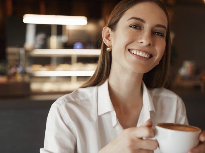 Close-up portrait happy alluring lady in white blouse, smiling cheerfully as sitting in cafe, businesswoman drinking coffee, relaxed rejoicing woman winning deal in court, have break.