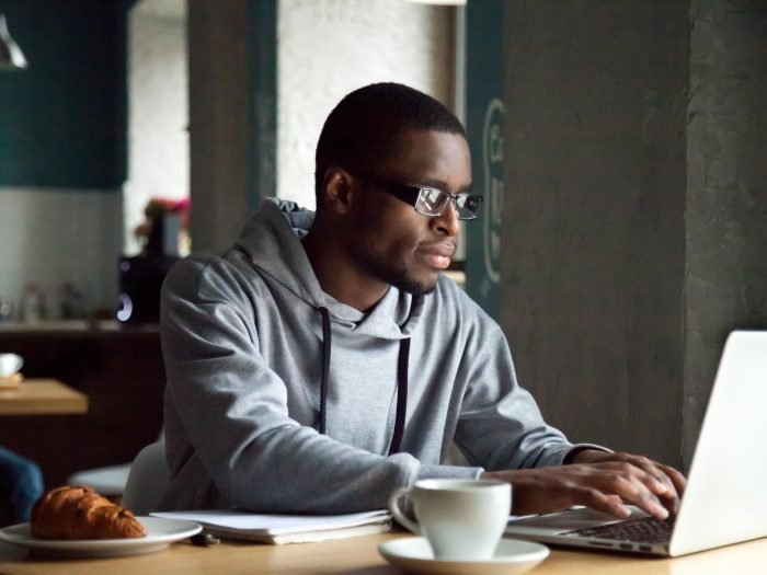 Serious millennial african-american man using laptop sitting at