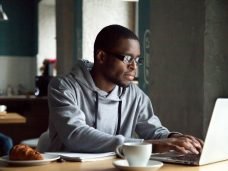 Serious millennial african-american man using laptop sitting at