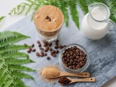 Top view of dalgona coffee with almond milk and brown sugar, coffee beans and green plant on marble board. A glass of trendy fluffy Korean drink with whipped cream.